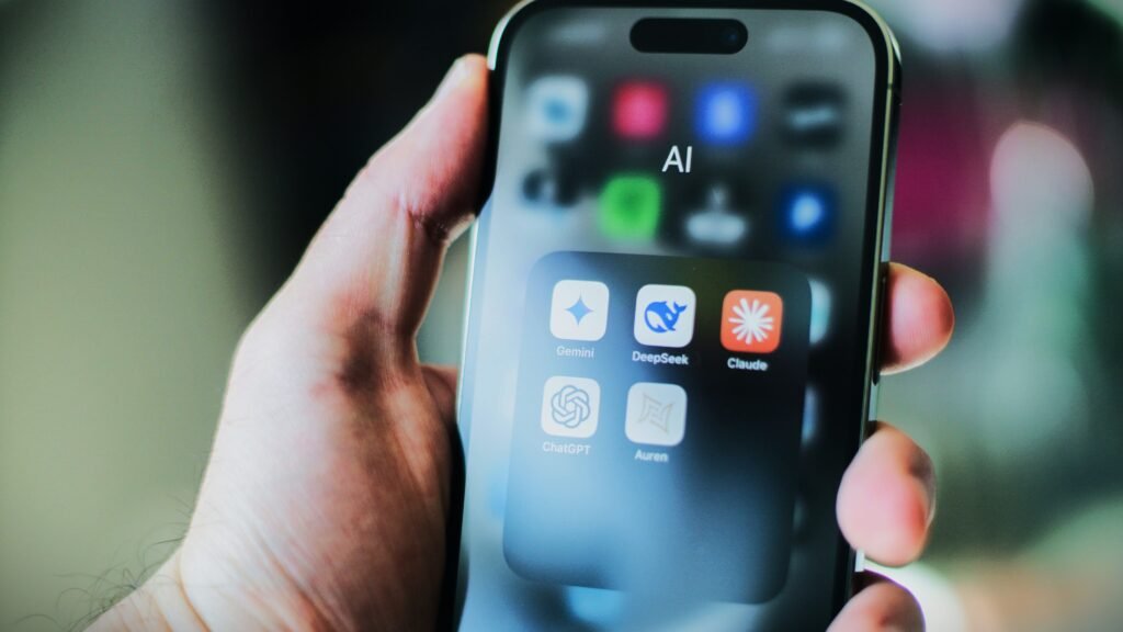 Hand holding an iPhone with an open folder showing top ai apps like ChatGPT, Gemini, Claude, and DeepSeek